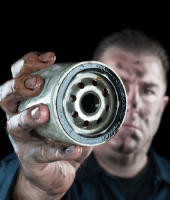 A man holding up an oil filter in front of his face.